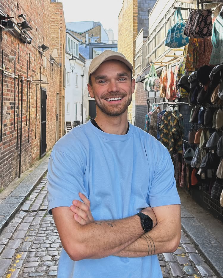 Laurie Shaw, smiling with his arms folded, standing in a cobbled market laneway.